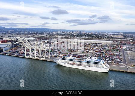 Oakland, Stati Uniti - 11 maggio 2020: Vista aerea di una nave da crociera ancorata al porto di Oakland, il suo brillante scafo bianco che contrasta con le acque blu profonde e il paesaggio industriale. Foto Stock