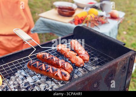 Salsicce grigliate fritte e succose su una griglia a fuoco nudo in primo piano. Picnic autunnale nella natura. Foto Stock