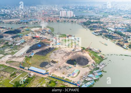 Dacca, Bangladesh - 11 settembre 2025: Vista aerea del fiume Buriganga, con cantieri di carbone in contrasto con l'acqua, i moli e il lontano skyline della città. Foto Stock