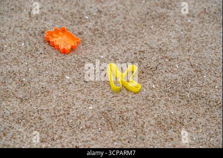 In una giornata calda e soleggiata, un paio di infradito gialli si riposa comodamente su una spiaggia sabbiosa, immergendosi nei raggi del sole Foto Stock