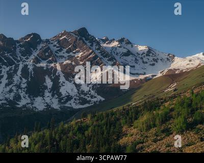Vista aerea delle maestose montagne che sorgono, le loro vette innevate baciate dal sole dorato, che si affacciano sui paesaggi di Biskeri Top, Sosan, Himachal Pradesh, India. Foto Stock