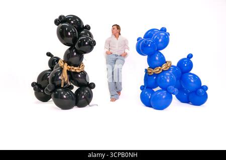 Una donna sta di fronte a due cani fatti di palloncini. Un cane è nero e l'altro è blu Foto Stock