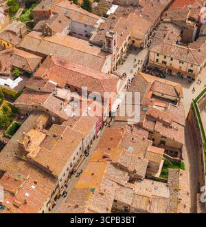 Vista aerea dei tetti di terracotta che cadono giù, una torre medievale alta tra antichi edifici in pietra e strade trafficate, San Quirico d'Orcia, Toscana, Italia. Foto Stock