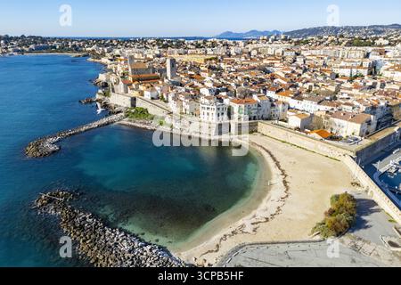 Veduta aerea della spiaggia di Plage de la Gravette baciata dal sole in contrasto con lo storico castello Grimaldi e l'azzurro Mar Mediterraneo, Antibes, Prov Foto Stock
