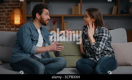 Coppia caucasica che parla a casa marito emotivo che condivide notizie incredibili con la moglie due persone fidanzata multirazziale fidanzato talk man donna ispanica Foto Stock