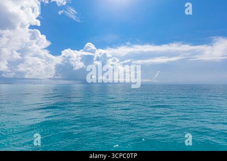 Splendida vista sull'oceano blu con cielo soleggiato, nuvole morbide e riflessi del cielo in superficie. La vivacità ispira la tranquillità del paesaggio marino tropicale Foto Stock