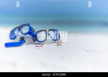 Primo piano dell'attrezzatura da snorkeling sulla spiaggia estiva. Maschera, boccaglio attività ricreative all'aperto. Mare, cielo e orizzonte sfocati. Natura morta astratta in sabbia soleggiata Foto Stock