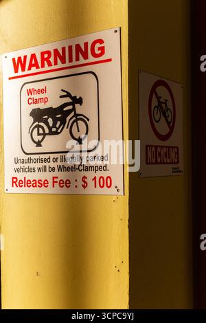 Vista verticale di una parete con cartello di avvertimento. I veicoli non autorizzati verranno bloccati con le ruote. Niente ciclismo. Effetto luce ed ombra. Singapore Foto Stock