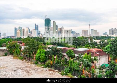 Vista dello skyline di Makati City con edifici del quartiere finanziario centrale sullo sfondo e un villaggio recintato con alberi in primo piano Foto Stock