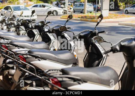 Una fila di scooter parcheggiati ordinatamente lungo la strada in un vivace ambiente cittadino. I veicoli sono visibili sullo sfondo, mostrando l'atmosfera vivace Foto Stock