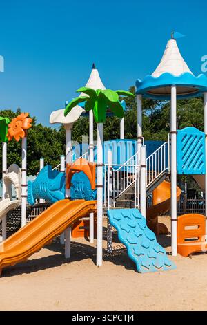 Parco giochi dai colori vivaci con numerosi scivoli e aree per arrampicate, circondato da alberi. Luogo ideale per i bambini per giocare ed esplorare all'aperto Foto Stock