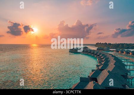 Fantastica vista aerea delle nuvole di cielo e tramonto del lussuoso resort delle Maldive. Ville sull'acqua che si affacciano sulla baia laguna oceanica, esotica destinazione estiva per vacanze tropicali. Foto Stock