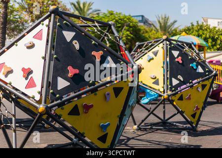 Strutture per arrampicate dai colori vivaci si trovano in un vivace parco giochi all'aperto circondato da palme. I bambini possono esplorare e giocare in un ambiente divertente e sicuro Foto Stock