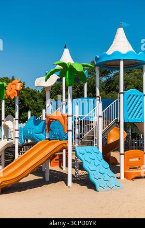 Parco giochi dai colori vivaci con numerosi scivoli e aree per arrampicate, circondato da alberi. Luogo ideale per i bambini per giocare ed esplorare all'aperto Foto Stock