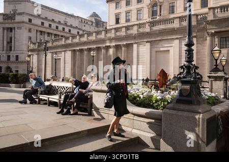 Una signora che indossa un cappello parla sul suo smartphone mentre aspetta fuori dal Royal Exchange, di fronte all'ingresso della Bank of England, City of London, Regno Unito Foto Stock