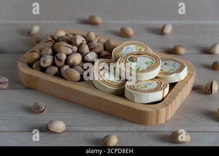 Primo piano di halva tradizionale a strati con pistacchi e un mucchio di pistacchi arrostiti su un vassoio di legno Perfetto per dolci culinari e orientali, ve Foto Stock