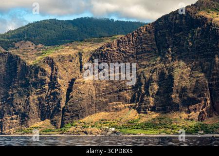 Una vista panoramica di una maestosa e ripida parete rocciosa che si innalza direttamente dal mare calmo e grigio-blu, con i suoi pendii superiori ricoperti da una fitta foresta verde e. Foto Stock