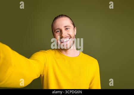 Attraente giovane uomo sorridente in una vivace camicia gialla con sfondo verde che crea un'atmosfera casual e positiva Foto Stock