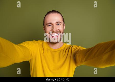 Bel giovane uomo in camicia gialla che fa allegri selfie davanti allo sfondo cachi per un concetto di stile di vita Foto Stock