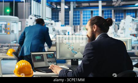Il tecnico di fabbrica del fotovoltaico regola i parametri del sistema sul computer portatile per massimizzare la generazione di energia dalle celle solari. Uomo che utilizza un notebook che ottimizza l'alimentazione di energia nello stabilimento di produzione di pannelli solari, fotocamera A. Foto Stock
