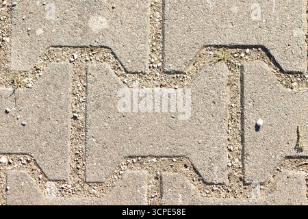 Colpo d'aria di asfaltatrici a forma di i in calcestruzzo con ghiaia nei giunti. Alcune lame d'erba sbirciano attraverso le crepe. Foto Stock