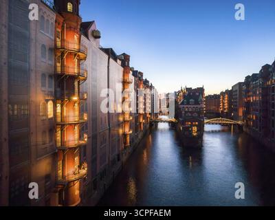 Vista serale del quartiere dei magazzini di Amburgo con vista del castello scavato dal fossato di Poggenmuehlenbruecke, circondato da magazzini in mattoni illuminati Foto Stock