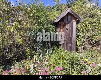 Una piccola casa in legno nel giardino con un simbolo del cuore sulla porta Outhouse, circondata da piante e fiori, Weinviertel bassa Austria Austria Austria Foto Stock