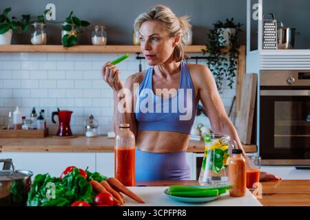 Promuovendo sane abitudini alimentari, una donna anziana sorridente ama un sedano fresco nella sua cucina, abbracciando uno stile di vita vivace e attivo Foto Stock