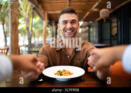 Esperienza culinaria, un uomo sorridente condivide felicità e cibo a tavola, risate e insieme Foto Stock