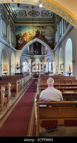 Riga, Lettonia - 2023-07-08 - momento religioso di meditazione e unità con Dio. Uomo solitario seduto su una panchina di legno all'interno della chiesa cattolica Foto Stock