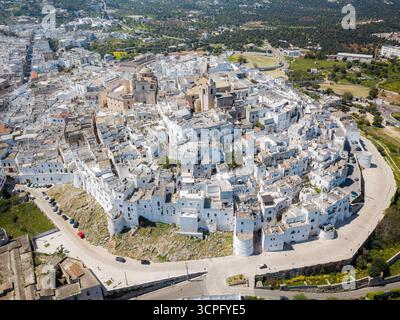 Veduta aerea dei radiosi edifici bianchi che scendono giù dalla collina, un netto contrasto con il verde paesaggio circostante, Ostuni, Puglia, Italia. Foto Stock