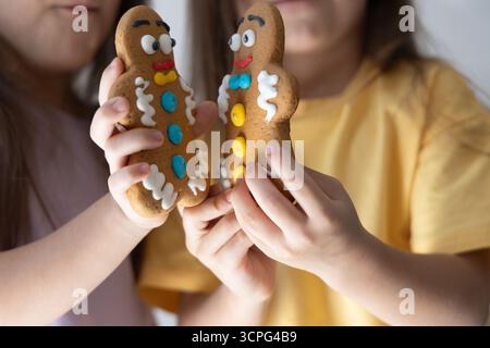 Due bambini tengono i biscotti dell'uomo di pan di zenzero vicini l'uno all'altro. Festività natalizie con bambini e dolciumi al forno che simboleggiano il Natale e. Foto Stock
