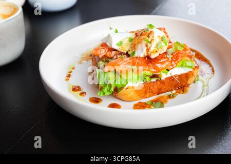 Un toast gourmet a vista comprende salmone affumicato, formaggio cremoso, verdure croccanti ed erbe fresche sopra il pane tostato, rifinito con un getto d'acqua e un luminoso Foto Stock