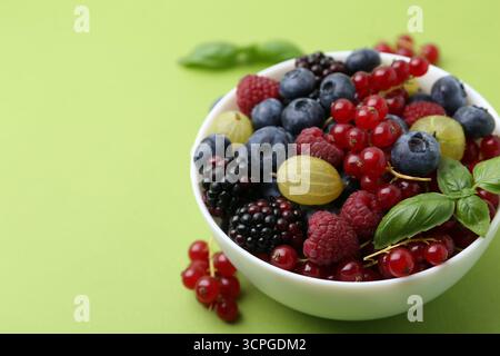 Diversi frutti di bosco e basilico maturi in ciotola su sfondo verde, primo piano. Spazio per il testo Foto Stock