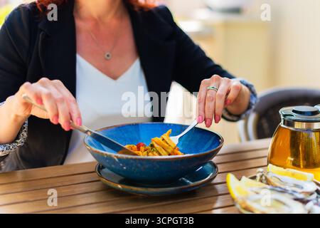 Donna seduta al tavolo da pranzo con posate, spaghetti bolognesi appena serviti e gusta il suo pasto al ristorante Foto Stock