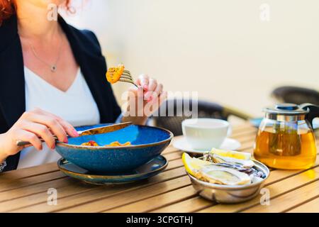 Donna seduta al tavolo da pranzo con posate, spaghetti bolognesi appena serviti e gusta il suo pasto al ristorante Foto Stock
