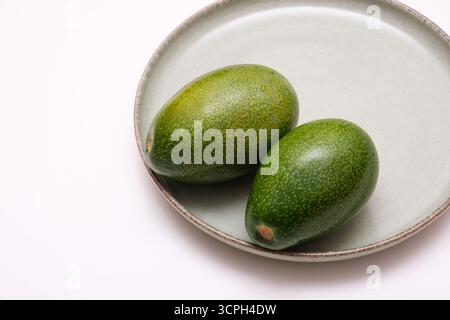 Due avocado maturi su un piatto verde. Avocado freschi su un piatto in ceramica, isolato su sfondo bianco. Foto Stock
