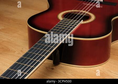 Una chitarra in stile vintage con una ricca finitura marrone rossastro, appoggiata su una superficie in legno. Sfoggia dettagli complessi con finiture Sunburst. Foto Stock