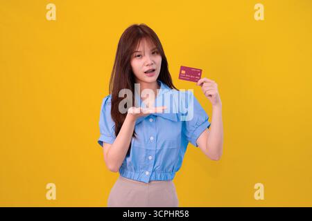 Giovane donna con carta di credito in Bright Yellow Studio sullo sfondo per shopping e concetto di pagamento Foto Stock