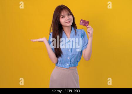 Giovane donna con carta di credito in Bright Yellow Studio sullo sfondo per shopping e concetto di pagamento Foto Stock