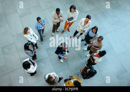 Un gruppo diversificato di professionisti viene visto dall'alto, formando un cerchio durante una riunione coinvolgente. L'immagine acquisisce una collaborazione e include Foto Stock