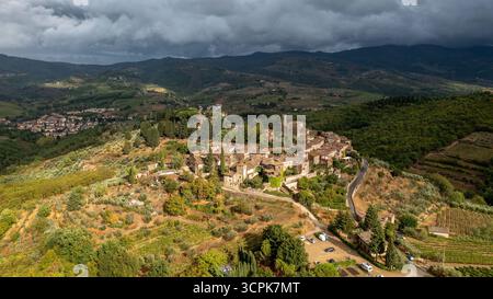 Vista aerea di un villaggio medievale annidato tra colline e vigneti ondulati, una sinfonia di tetti ocra e paesaggi verdeggianti, Greve in Chiant Foto Stock