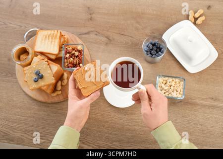 Giovane con tazza di tè e brindisi con burro di arachidi in cucina, primo piano Foto Stock