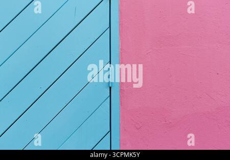 Porta in legno diagonale blu accostata a una parete liscia e rosa. Le tavole della porta sono disposte meticolosamente in diagonale. Foto Stock
