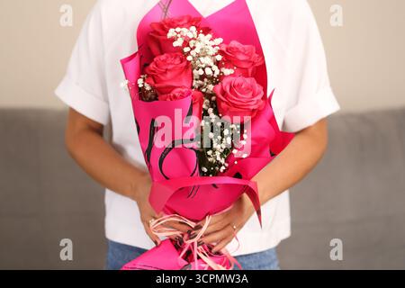 Bouquet di rose avvolto in carta rosa. Persona che regge un regalo di fiori. Regalo romantico per festeggiare. Composizione floreale con decorazione. Foto Stock