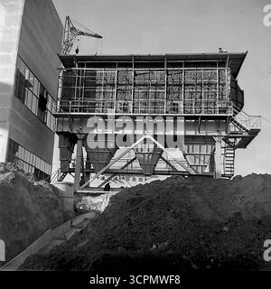 Una grande tramoggia industriale è raffigurata in costruzione nel sito di un impianto di calce e gesso a Shyldivka, RSS Ucraina, negli anni '1970 Questa foto monocromatica di archivio cattura una fase chiave di una "stroyka" sovietica, che mostra l'installazione di pannelli isolanti sull'ampia unità di filtrazione o stoccaggio. La scena, con una gru sullo sfondo e la terra scavata in primo piano, è una testimonianza dell'industria pesante della regione del Donbas Foto Stock
