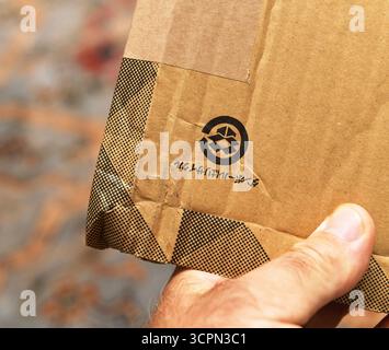 Parigi, Francia - 8 agosto 2025: Primo piano di una mano che tiene in mano una confezione di cartone marrone Amazon prime Japan con simbolo di riciclaggio e testo giapponese Foto Stock