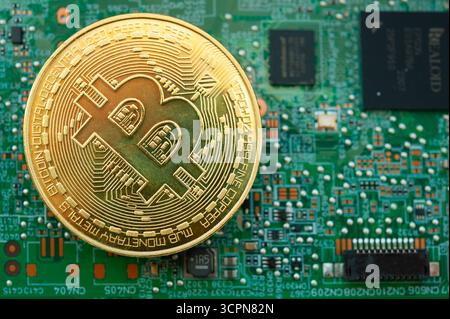 Moneta Bitcoin d'oro sulla scheda madre del computer che simboleggia il mining di criptovalute e la finanza digitale Foto Stock