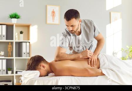 Massaggio maschile mirato che esegue un massaggio alla schiena su un paziente Foto Stock