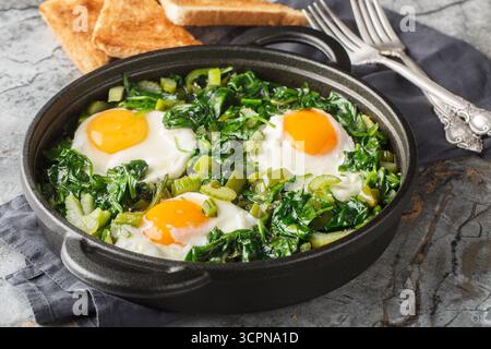 Lo shakshuka verde è uno stufato di uova in una miscela di verdure verdi ed erbe aromatiche, primo piano in una padella su un tavolo. Orizzontale Foto Stock